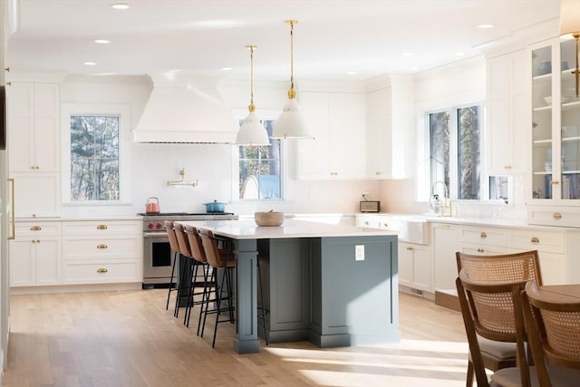 kitchen with a center island, a breakfast bar area, custom range hood, high end stainless steel range oven, and white cabinetry