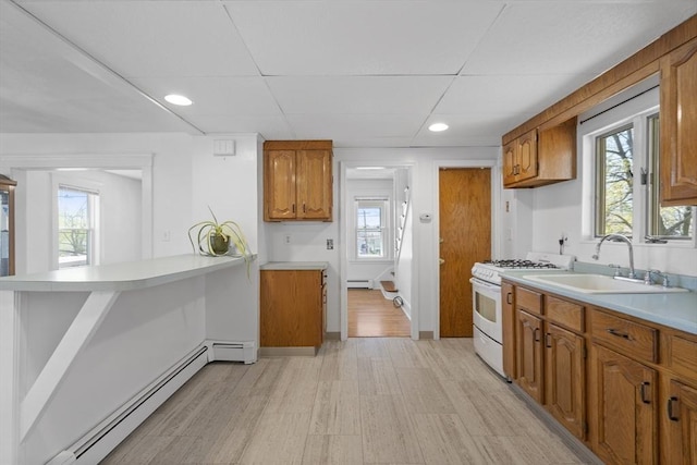 kitchen featuring white range with gas cooktop, baseboard heating, a sink, brown cabinets, and recessed lighting