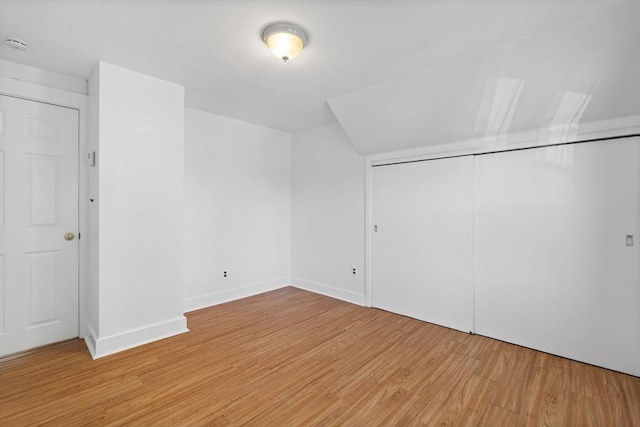 unfurnished bedroom with light wood-style floors, a closet, baseboards, and vaulted ceiling