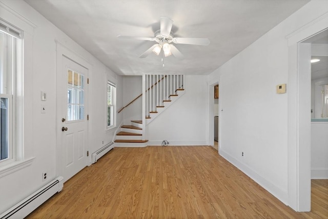foyer entrance with baseboard heating, stairway, light wood-style floors, and ceiling fan