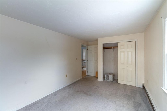 unfurnished bedroom with carpet floors, a baseboard heating unit, and a closet