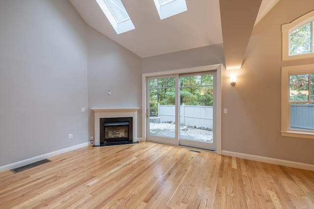108 Johnson Woods Unit 108, Reading, MA 01867 - unfurnished living room featuring high vaulted ceiling, a skylight, a fireplace with flush hearth, and light wood-type flooring