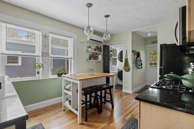 63-65 Brookley Rd Unit 3, Boston, MA 02130 - kitchen featuring stacked washer / drying machine, stainless steel microwave, freestanding refrigerator, a wall mounted air conditioner, and light wood finished floors