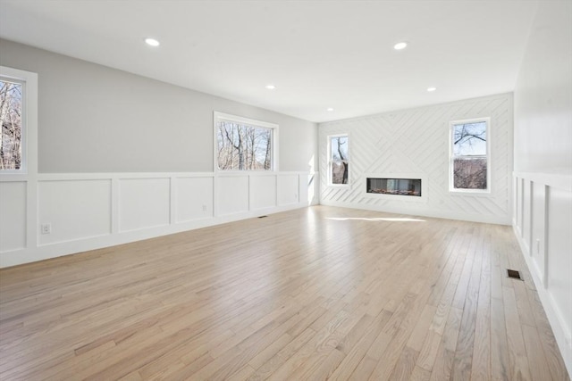 1 Falcon Dr, Shrewsbury, MA 01545 - unfurnished living room featuring healthy amount of natural light, a decorative wall, light wood-style floors, a glass covered fireplace, and wainscoting