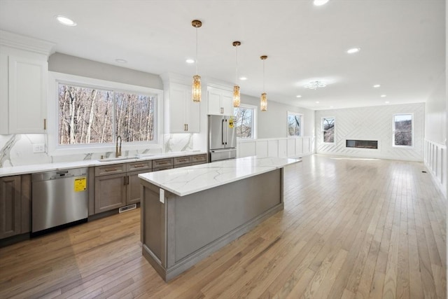 1 Falcon Dr, Shrewsbury, MA 01545 - kitchen featuring stainless steel appliances, light wood-type flooring, a glass covered fireplace, a kitchen island, and light stone countertops