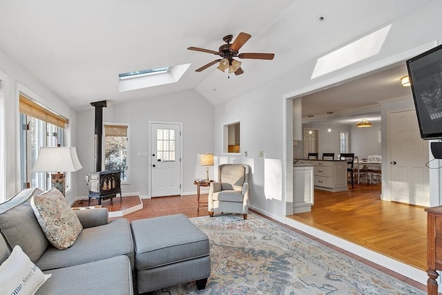 living room featuring a wood stove, lofted ceiling with skylight, ceiling fan, and light wood-type flooring