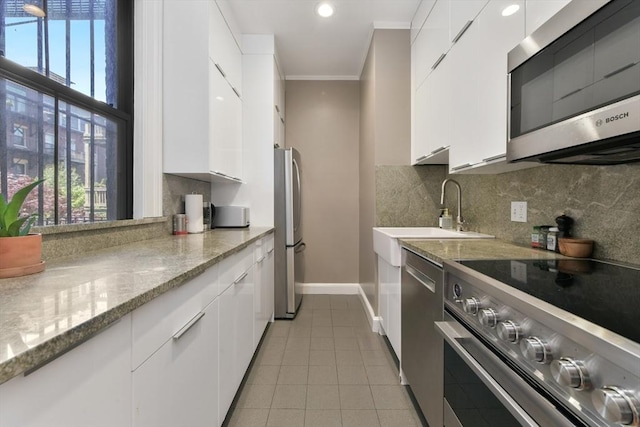 kitchen with a sink, stainless steel appliances, white cabinetry, and light tile patterned flooring