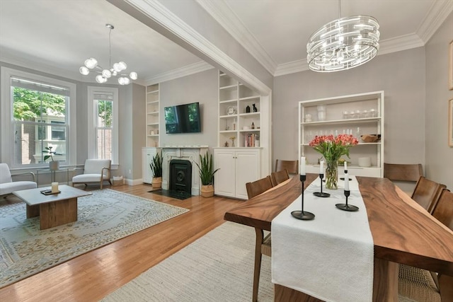 dining area featuring wood finished floors, built in shelves, a chandelier, crown molding, and baseboards