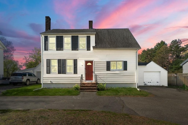 colonial home with a chimney, an outbuilding, a detached garage, fence, and aphalt driveway