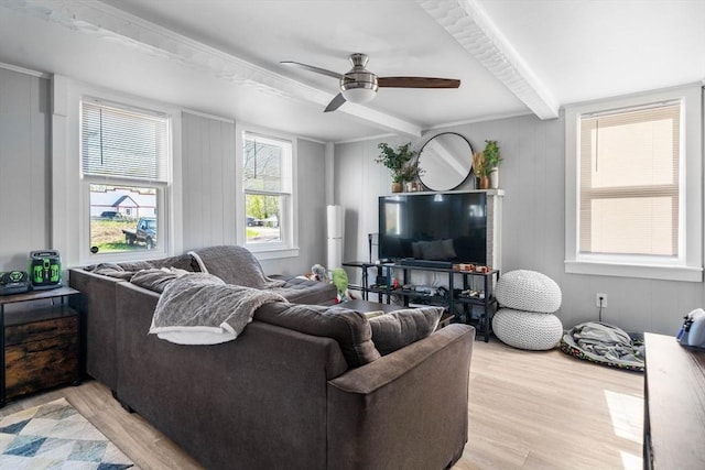 living area with a decorative wall, a ceiling fan, beam ceiling, and light wood-style floors