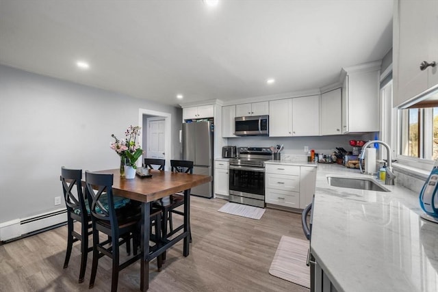 kitchen featuring light stone counters, appliances with stainless steel finishes, a sink, recessed lighting, and a baseboard radiator