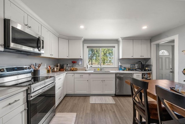 kitchen with appliances with stainless steel finishes, a sink, light countertops, white cabinetry, and light wood-type flooring