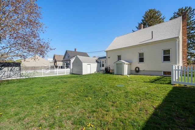 rear view of house featuring a yard, an outdoor structure, a fenced backyard, and a storage unit