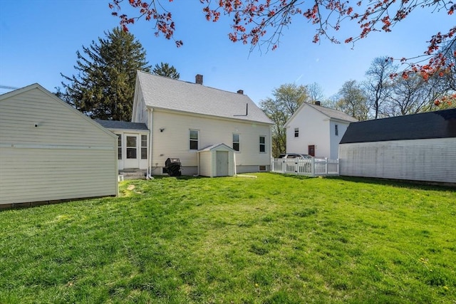 back of house with a chimney, fence, an outdoor structure, a storage unit, and a yard