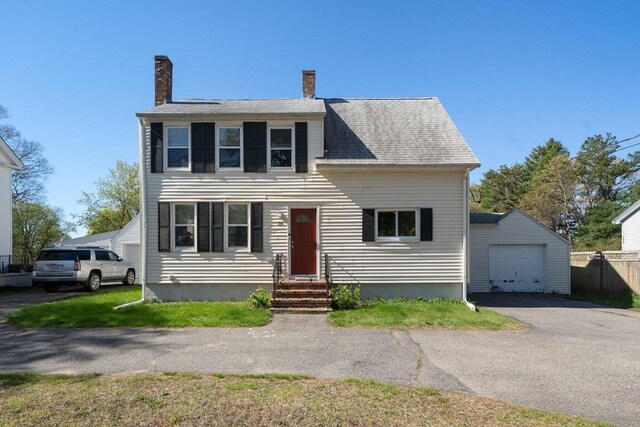 colonial house with aphalt driveway, a garage, entry steps, an outbuilding, and a chimney