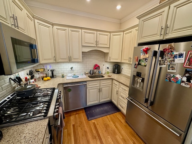 kitchen featuring appliances with stainless steel finishes, tasteful backsplash, ornamental molding, sink, and light hardwood / wood-style flooring