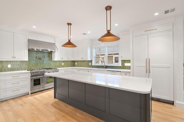 kitchen featuring visible vents, white cabinets, wall chimney range hood, light wood-type flooring, and double oven range