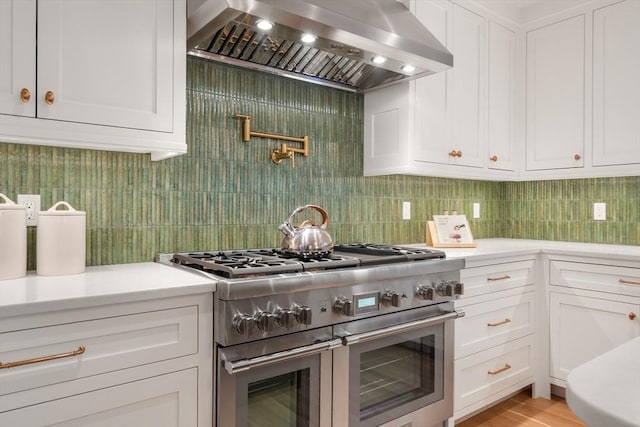 kitchen featuring wall chimney exhaust hood, double oven range, light countertops, and backsplash