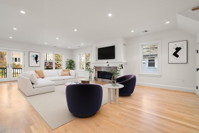 living area featuring light wood finished floors, french doors, a glass covered fireplace, and a healthy amount of sunlight