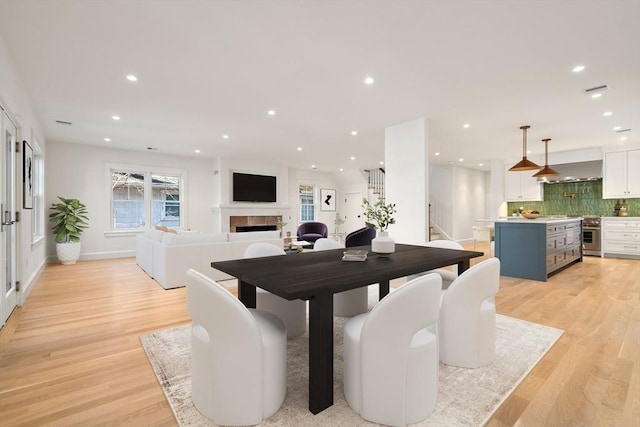 dining room with light wood-style flooring, a tile fireplace, stairway, and recessed lighting