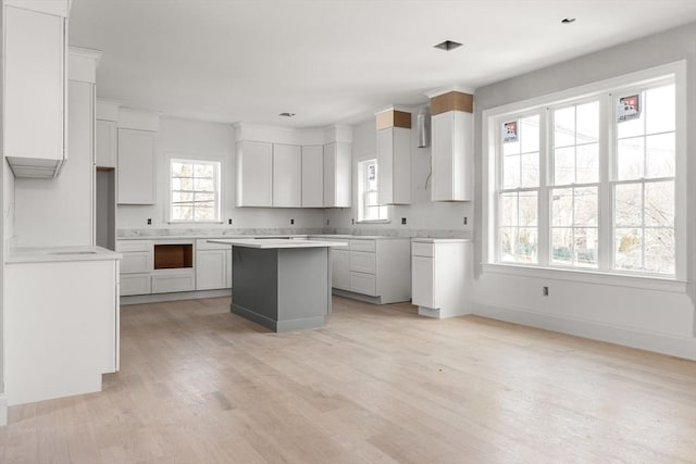 kitchen featuring baseboards, light wood-style flooring, a center island, light countertops, and white cabinetry