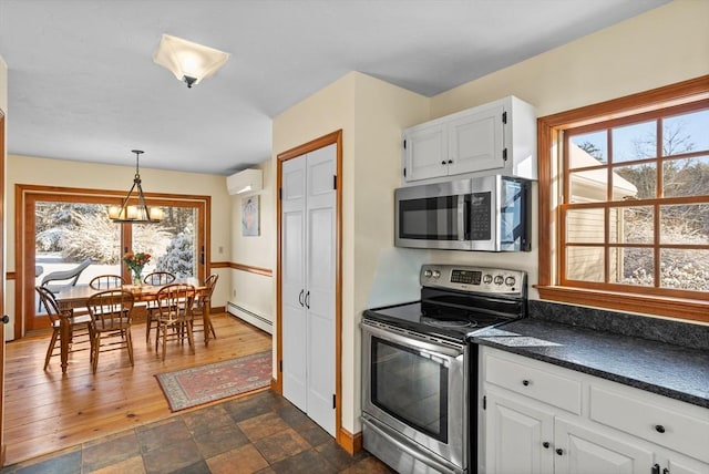 kitchen featuring white cabinetry, decorative light fixtures, an AC wall unit, stainless steel appliances, and a baseboard heating unit