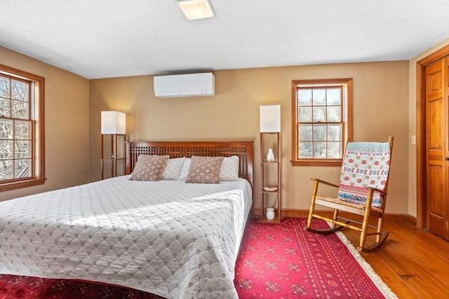 bedroom featuring a wall mounted air conditioner, wood-type flooring, and multiple windows