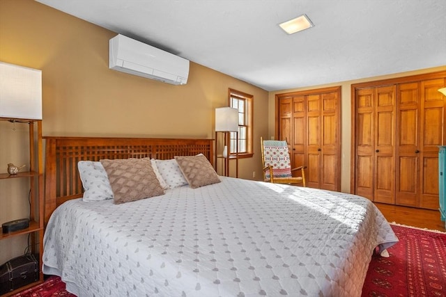 bedroom featuring hardwood / wood-style floors, two closets, and a wall unit AC