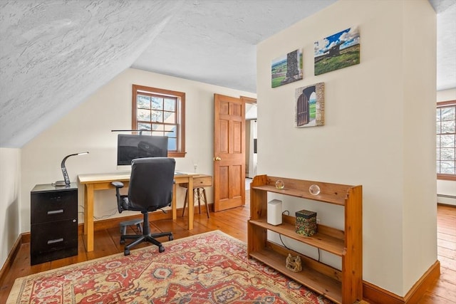 home office featuring lofted ceiling, light hardwood / wood-style floors, a textured ceiling, and a baseboard heating unit