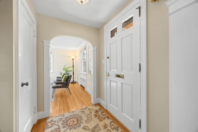 doorway featuring decorative columns, arched walkways, baseboards, radiator heating unit, and light wood-type flooring