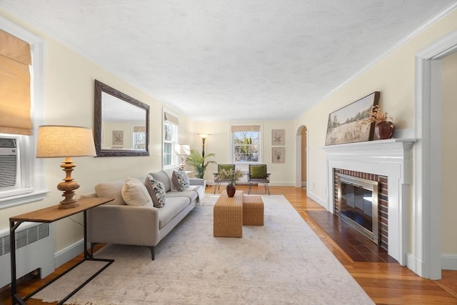 living room featuring arched walkways, a fireplace, wood finished floors, baseboards, and radiator