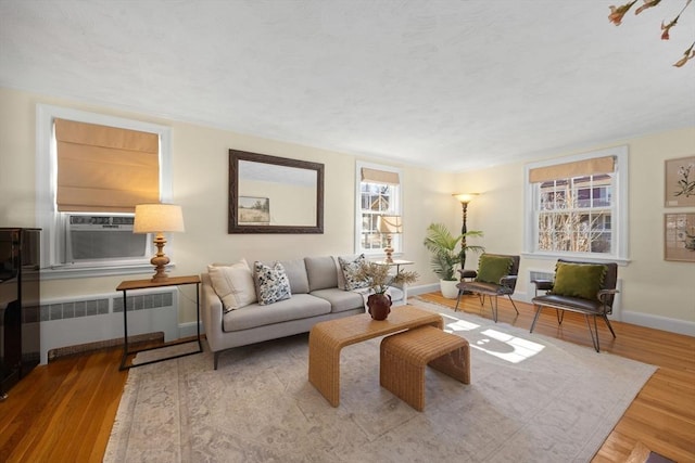 living room with baseboards, cooling unit, wood finished floors, and radiator