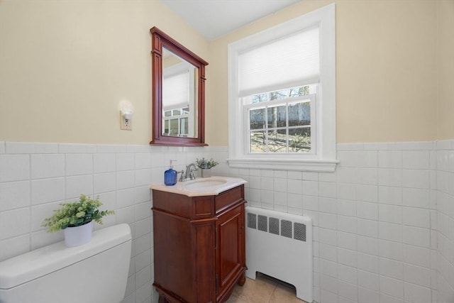 bathroom featuring tile patterned flooring, toilet, vanity, tile walls, and radiator heating unit