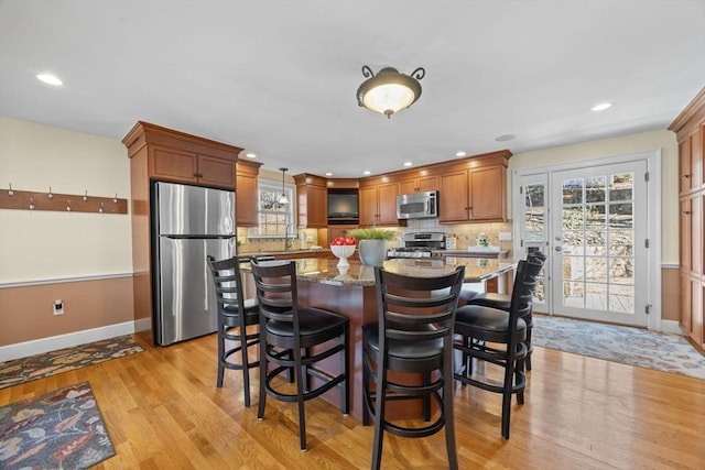 kitchen featuring a breakfast bar area, stainless steel appliances, tasteful backsplash, light wood-style flooring, and a kitchen island