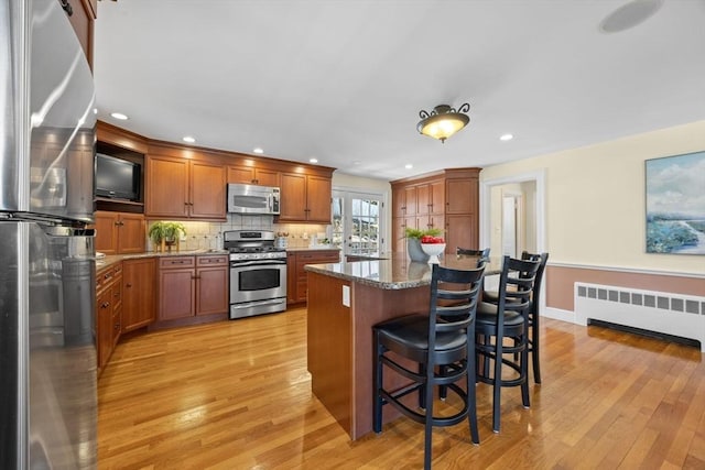 kitchen featuring a breakfast bar area, stainless steel appliances, backsplash, radiator heating unit, and light wood-type flooring