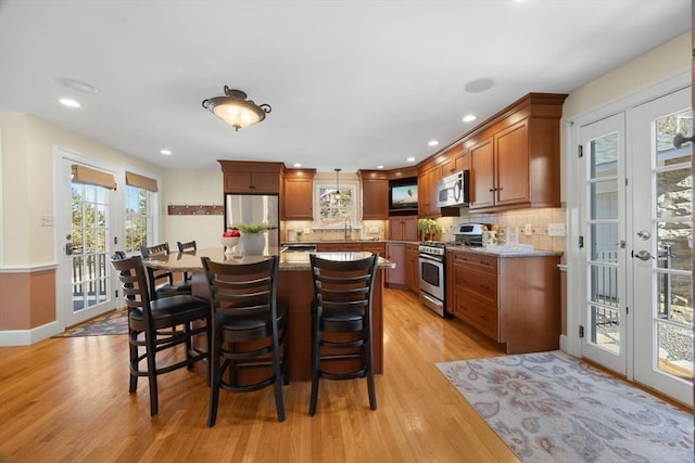 kitchen with a breakfast bar, french doors, appliances with stainless steel finishes, light wood finished floors, and tasteful backsplash