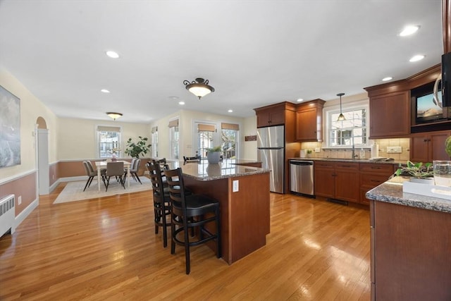 kitchen with stainless steel appliances, a kitchen breakfast bar, backsplash, a center island, and light wood finished floors