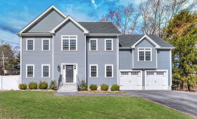 colonial home featuring a front lawn, driveway, fence, a shingled roof, and a garage