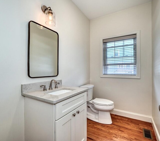 bathroom featuring visible vents, baseboards, toilet, wood finished floors, and vanity