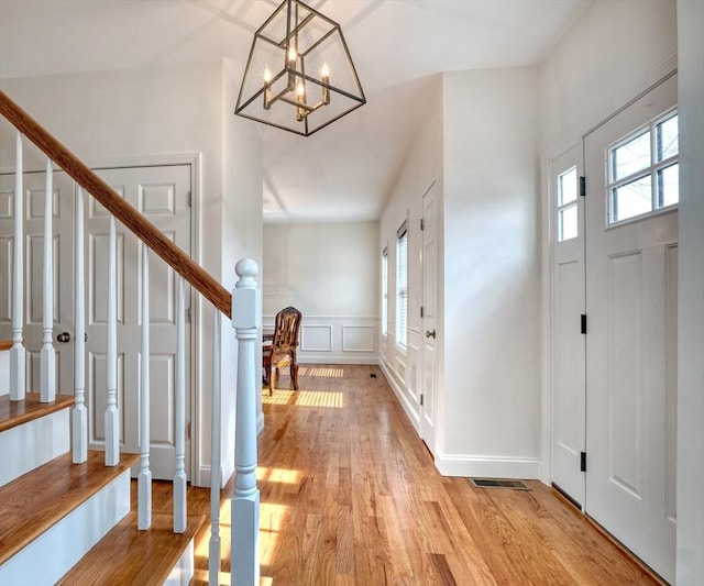 foyer with light wood finished floors, stairway, a wainscoted wall, an inviting chandelier, and a decorative wall