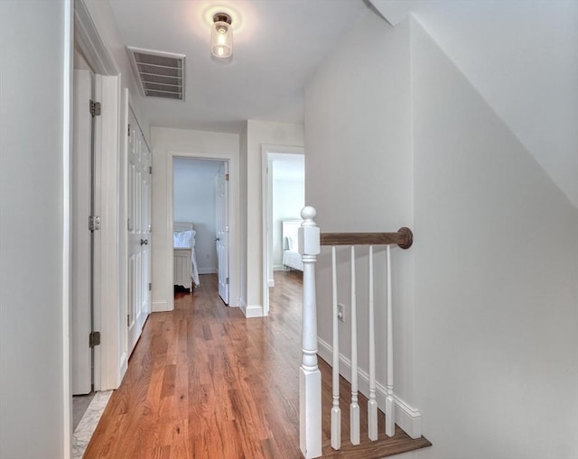 corridor with an upstairs landing, visible vents, light wood-type flooring, and baseboards