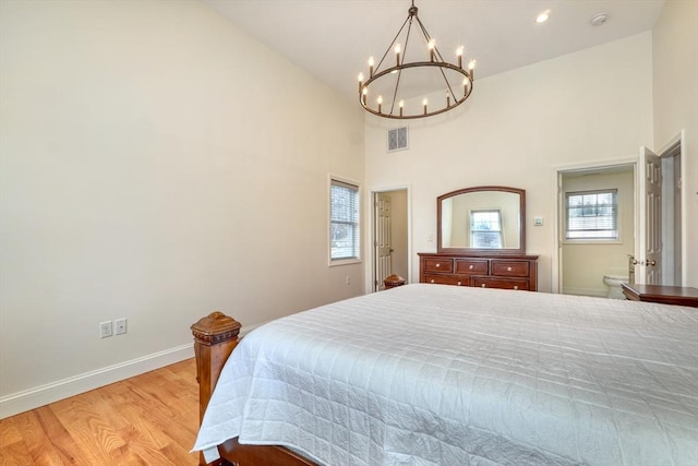 bedroom featuring visible vents, a notable chandelier, light wood finished floors, baseboards, and a towering ceiling