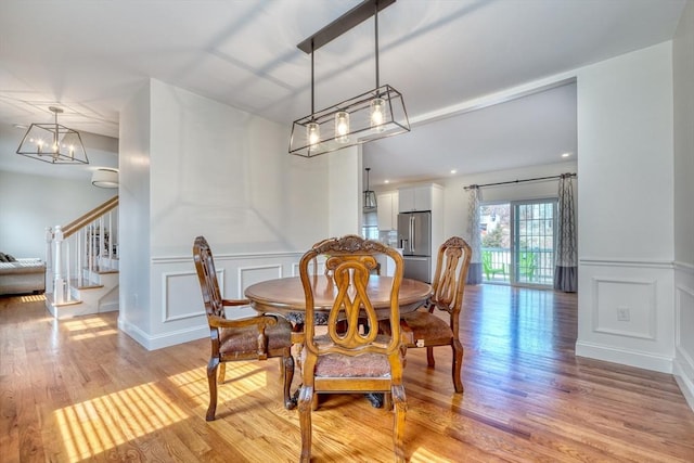 dining area featuring a decorative wall, wainscoting, stairs, and light wood finished floors