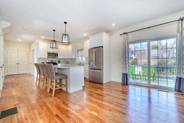 kitchen with visible vents, a kitchen island, light countertops, white cabinets, and stainless steel appliances