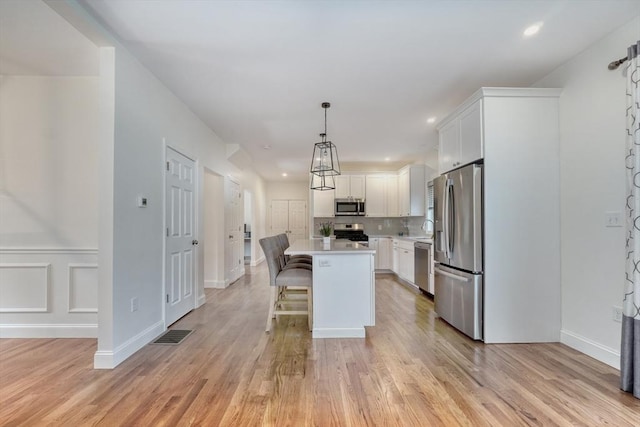 kitchen featuring a kitchen island, light wood-style flooring, stainless steel appliances, light countertops, and white cabinetry