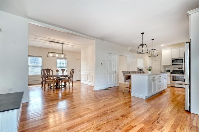 kitchen featuring a breakfast bar area, light wood-type flooring, light countertops, appliances with stainless steel finishes, and white cabinets