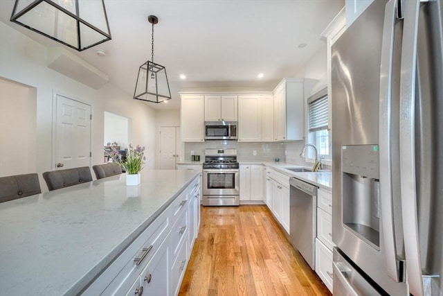 kitchen with light wood-style flooring, a sink, backsplash, appliances with stainless steel finishes, and hanging light fixtures