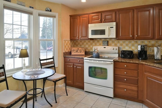 kitchen featuring decorative backsplash, light tile patterned floors, dark stone counters, and white appliances