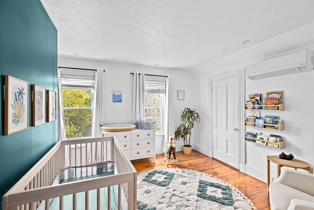 30 Highland St, Abington, MA 02351 - bedroom featuring a wall mounted AC, wood-type flooring, a textured ceiling, a nursery area, and baseboards