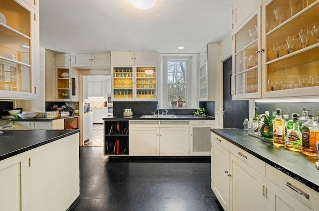 kitchen with dark countertops, a sink, glass insert cabinets, and recessed lighting